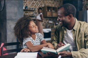 A father and daughter sitting together and reading a book.